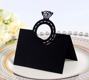 Close-up of laser-cut black place card featuring a diamond ring hollow design on white plate