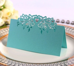Close-up of laser-cut heart pattern teal wedding place card on a white porcelain plate