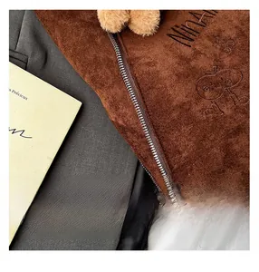 Gros plan sur sac en daim marron avec broderie pomme et détail de pompon doux