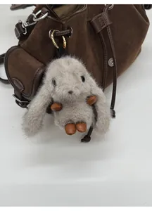 Close-up of a fluffy grey bunny plush keychain with gold ring on a suede handbag