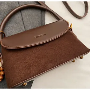 Detail view of dark brown suede and leather crossbody bag with brand embossing