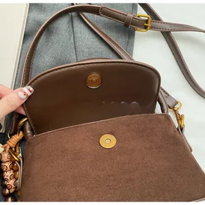 Close-up of brown suede crossbody bag with gold magnetic buckle and wooden bead detail