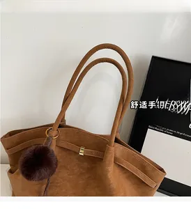 Detail of dark brown faux suede tote with slim shoulder straps and a plush pom-pom charm
