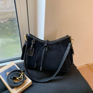 Detail of black suede shoulder bag with contrast stitching and golden metal buckles