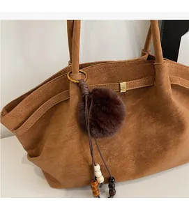 Close-up of caramel faux suede tote bag with plush ball charm and wooden bead tassel