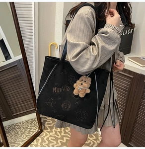 Détail d'un sac cabas en daim noir avec broderie, fermetures éclair et un charme d'ours