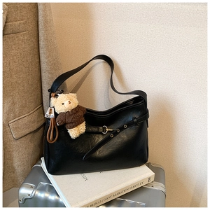 Détail du sac hobo en cuir noir avec un charmant ours en peluche sur un livre blanc