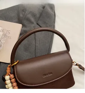 Close-up of brown leather bag featuring wooden bead charm and brand logo detail