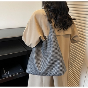 Detail of a large woven silver tote bag worn over the shoulder by a model in a trench coat