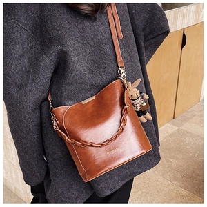 Detail of a brown leather bucket bag with braided handle and a cute rabbit charm