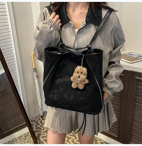 Détail d'un sac à dos en daim noir avec broderie et porte-clé ours en peluche marron