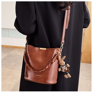 Detail of dark brown bucket bag with rabbit charm and adjustable shoulder strap on model