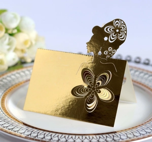 Laser cut gold seating card with female silhouette and flowers on a white porcelain plate