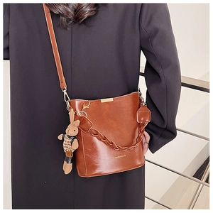 Detail view of brown leather bucket bag featuring woven handle and cute rabbit charm