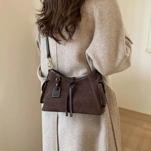 Detail of dark brown suede shoulder bag with side pockets on a beige cashmere coat