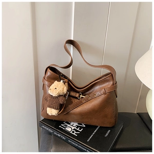 Détail d'un sac porté épaule marron texturé avec un charmant ours sur des livres