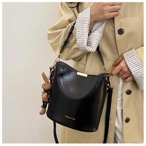 Detail of black patent leather bucket bag with woven handle and brown rabbit charm