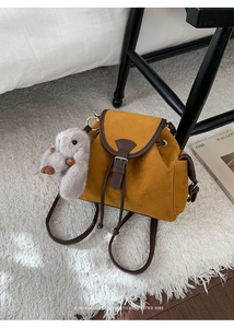 Detail of mustard yellow drawstring backpack with brown leather trim and plush rabbit charm