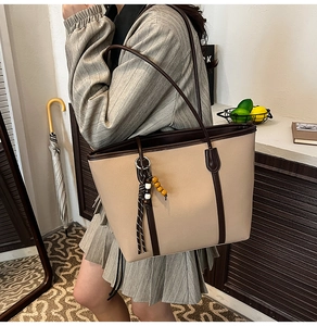 Detail of a large beige tote bag with brown trim and vintage wooden bead tassel accessory