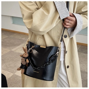 Detail of glossy black bucket bag with gold chain and plush rabbit charm on trench coat
