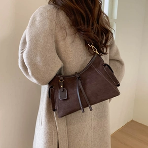 Detail of dark brown suede shoulder bag featuring white stitching and gold hardware