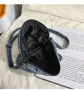 Detail view of denim crossbody bag interior with black fabric lining and silver zipper