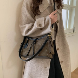 Detail of dark khaki suede shoulder bag with contrast stitching on wool coat