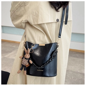 Model showing black bucket bag with a plush bunny charm and adjustable long strap