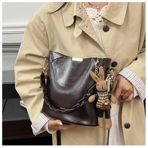 Detail of dark brown wavy textured bucket bag with woven handle and bunny pendant