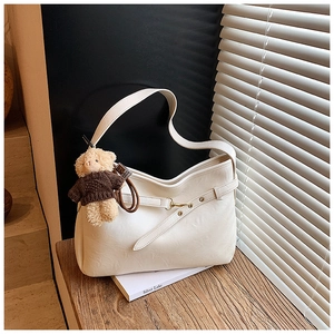 Détail d'un sac bandoulière crème avec boucle réglable et petit pendentif ours en peluche