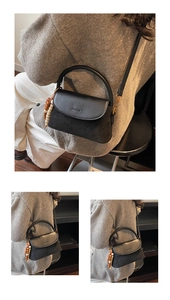 Detail of minimalist black crossbody bag with leather texture and bead charm