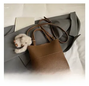 Close-up of brown lychee grain leather bucket bag with plush charm and long strap