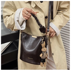 Detail of dark brown bucket bag with woven handle and plush rabbit pendant