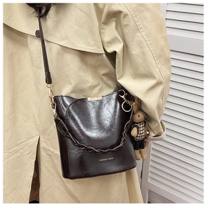 Detail of dark brown leather bucket bag featuring a woven handle and cute rabbit charm