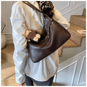 Détail d'un sac cabas en cuir marron foncé avec bandoulière réglable et breloque ourson