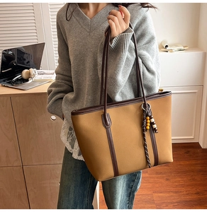 Detailed shot of large khaki tote bag with dark handles and a boho charm on a shoulder