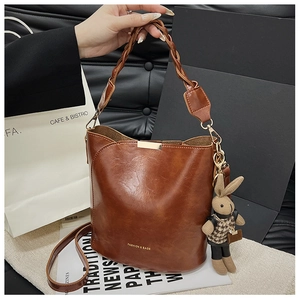Detail of a brown leather bucket bag with woven handle and plaid rabbit charm accessory