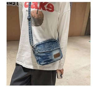 Détail d'un sac bandoulière en denim délavé avec logo en cuir vintage et bandoulière réglable