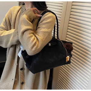 Detail of black suede tote bag with brown fur pompom and wooden bead tassel decoration