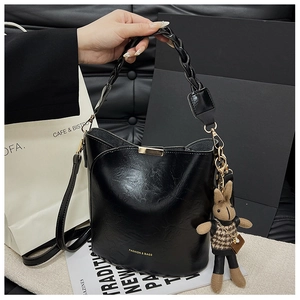 Detail of black leather bucket bag with woven handle and cute rabbit doll keychain