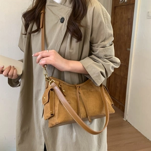 Close-up of brown suede crossbody bag with fringe detail worn with a beige trench coat