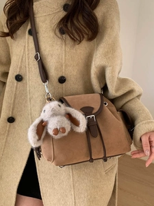 Caramel brown vintage crossbody bag with plush bunny charm on beige wool coat