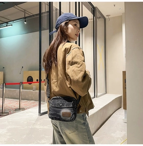 Détail d'un sac bandoulière en denim noir avec écusson en cuir Street Chic et sangle réglable