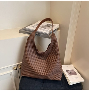 Detailed macro view of brown woven hobo bag with wide leather shoulder strap on stool
