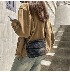 Détail du sac bandoulière en denim délavé avec écusson en cuir et poche à rabat