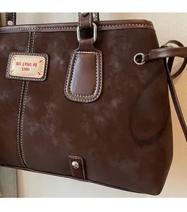 Close-up of dark brown suede tote bag featuring white contrast stitching and leather brand tag