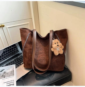 Détail de sac cabas en suédine marron foncé avec fermetures éclair et porte-clés ours