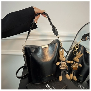 Detail of black textured bucket bag with woven handle and rabbit plush charm