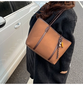 Detail of a large brown tote bag with wood bead tassel and leather trim in street style
