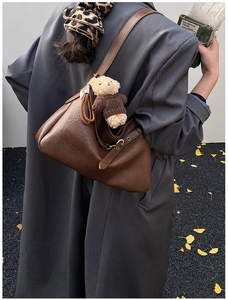 Détail d'un sac cabas vintage marron avec breloque ours sur un fond de manteau gris